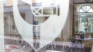 An outdoor seating area with tables and chairs, a glass balustrade, and a view of the street.