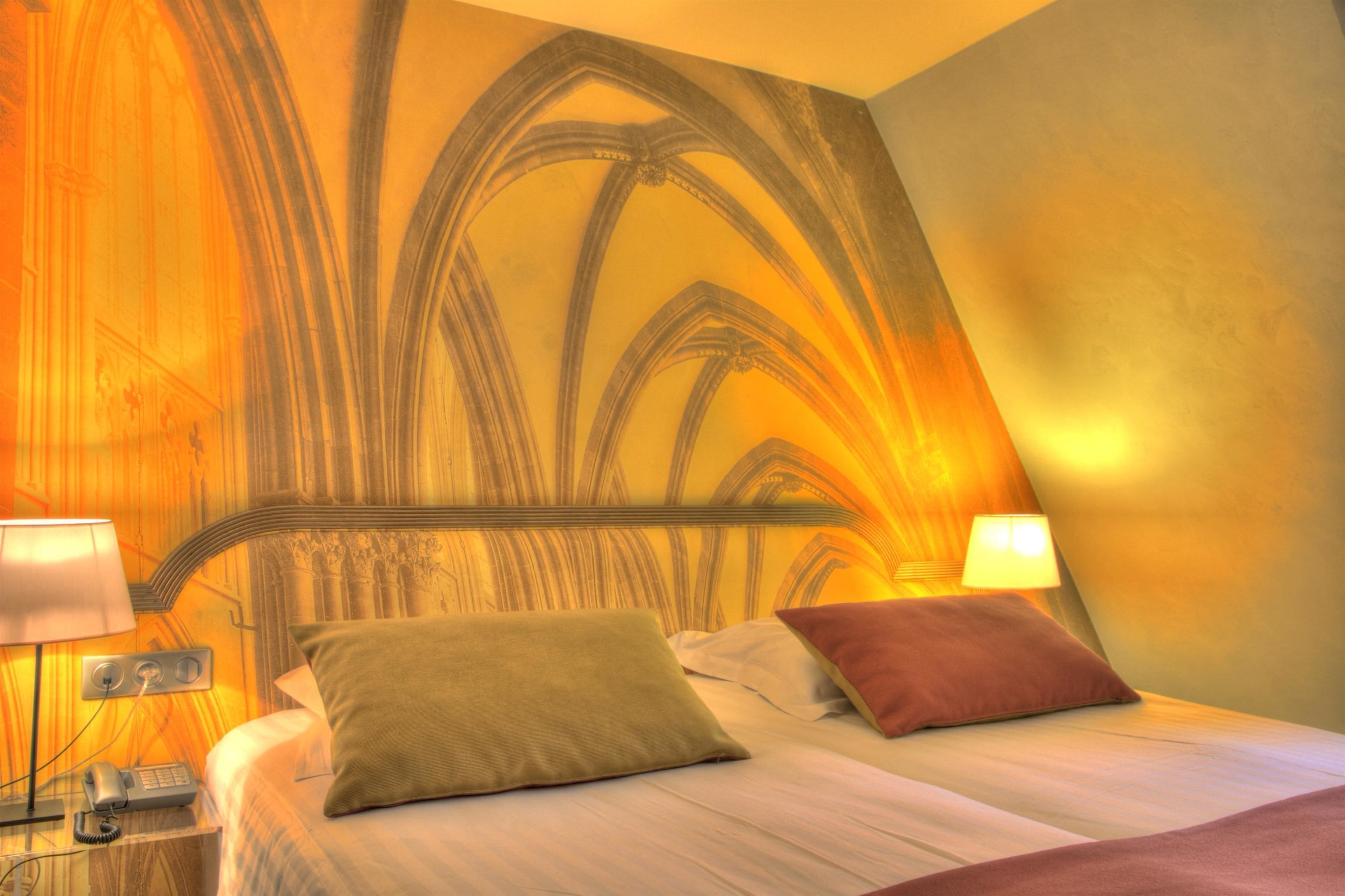 A hotel room with a large bed, two bedside lamps, and a decorative wall with a gothic arch design.