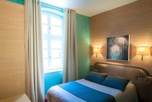 Habitación de hotel con cama, cortinas, un cuadro en la pared y dos lámparas de pared.