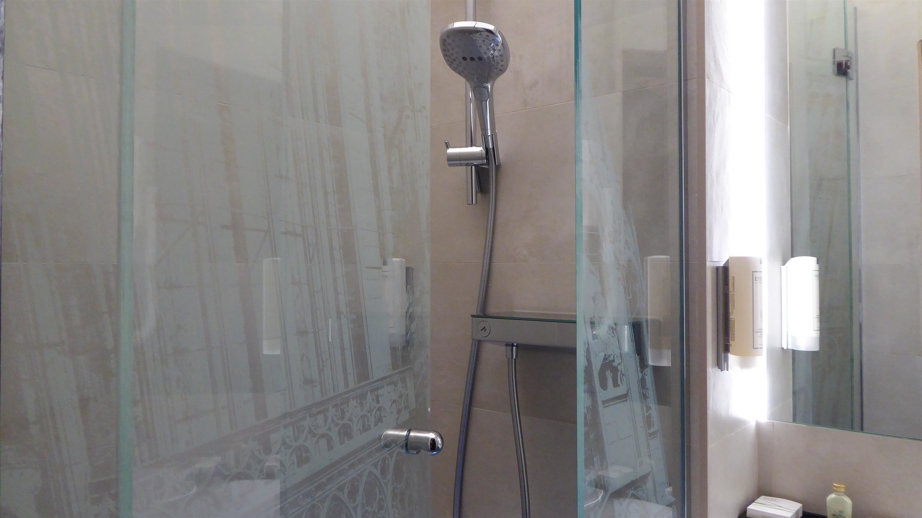 Une douche fermée par des parois en verre, dotée d’un pommeau de douche à main et d’un panneau de commande fixé au mur.