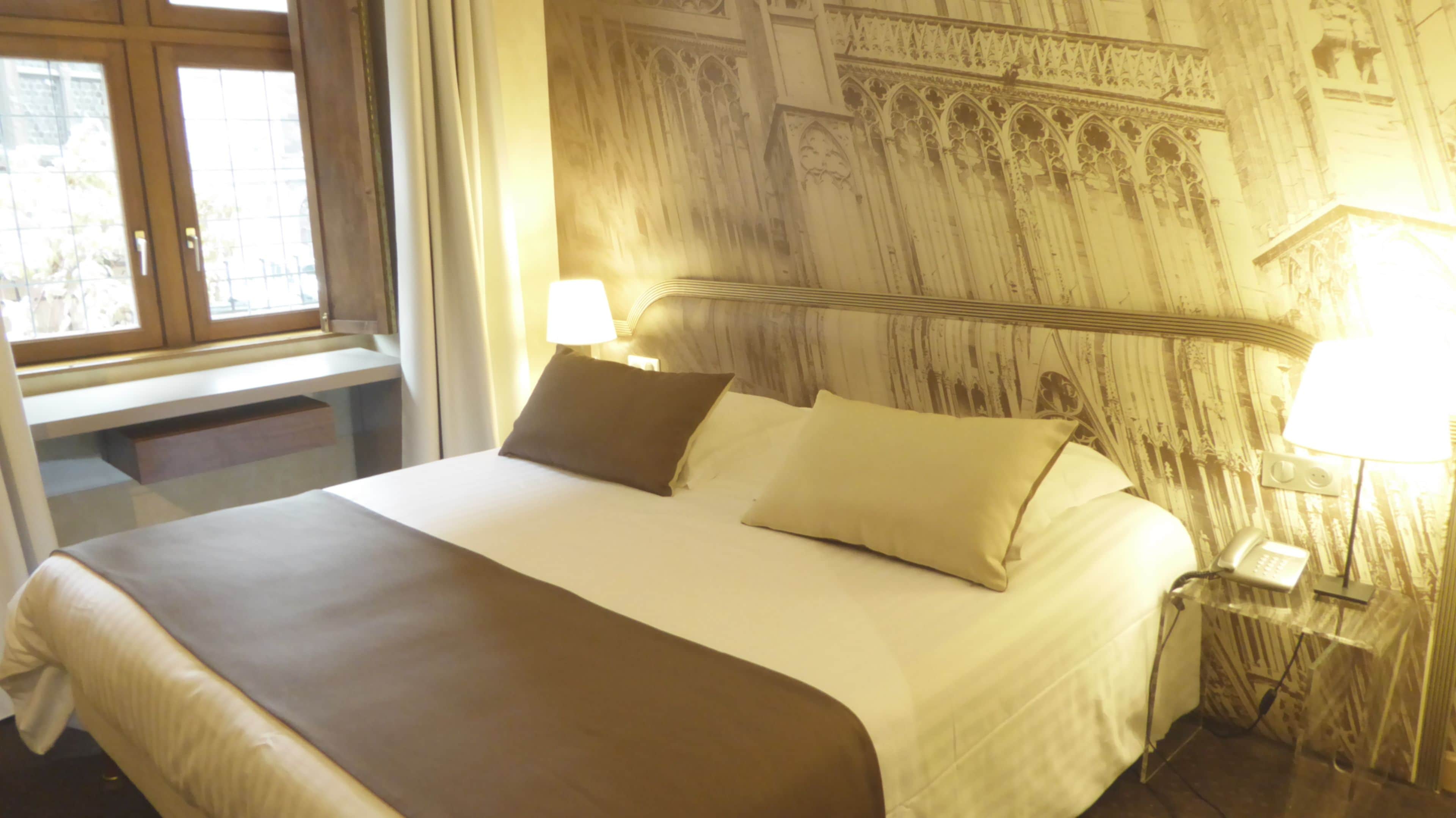 A hotel room with a large bed, two bedside lamps, and a window with curtains.