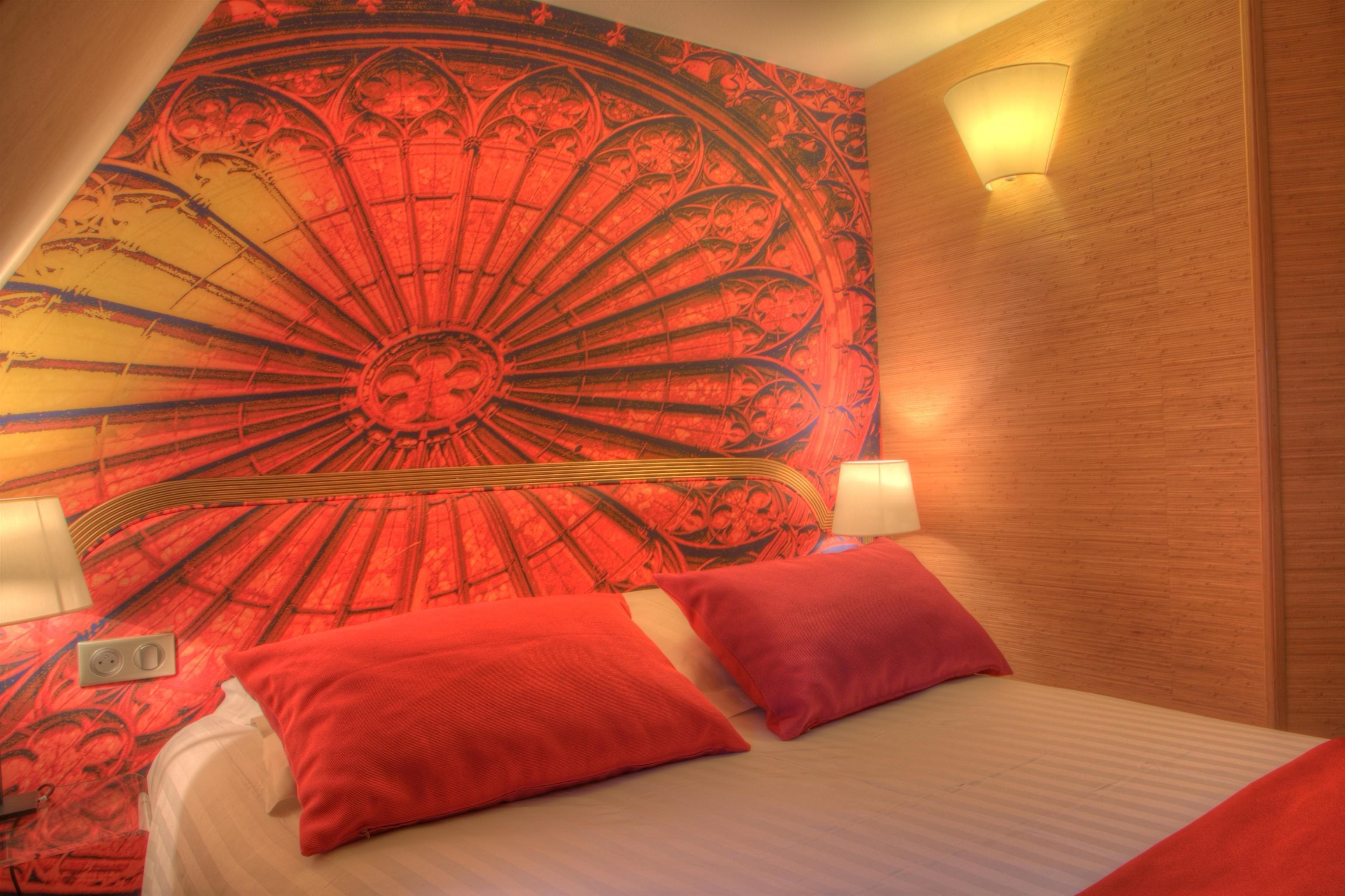 A bedroom with a large tapestry, two bedside lamps, and red pillows.