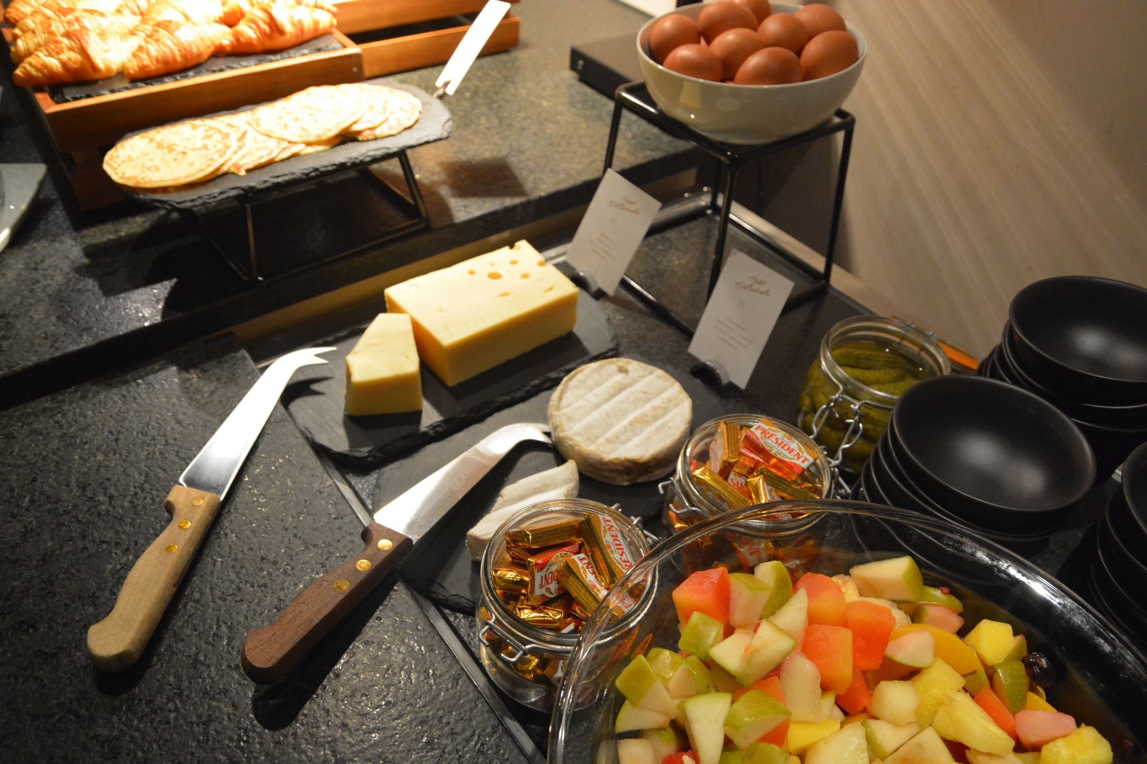 A buffet table with various food items including cheese, bread, eggs, and fruit.