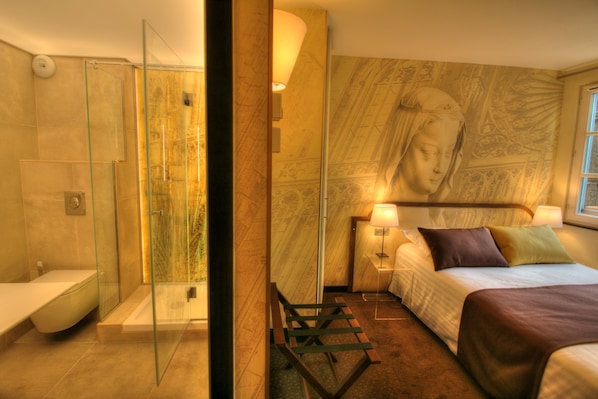 Ein modernes Hotelzimmer mit einer gläsernen Dusche, einem Bett mit Kopfteil und einem Wandgemälde.