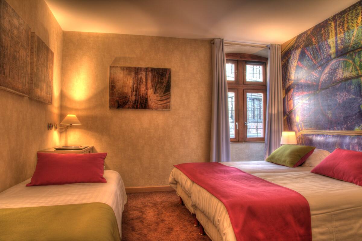 A hotel room with two beds, a large window, and a tapestry on the wall.