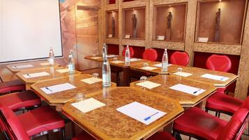 Ein Konferenzraum mit Holztischen und roten Stühlen, ausgestattet mit Wasserflaschen und Unterlagen.