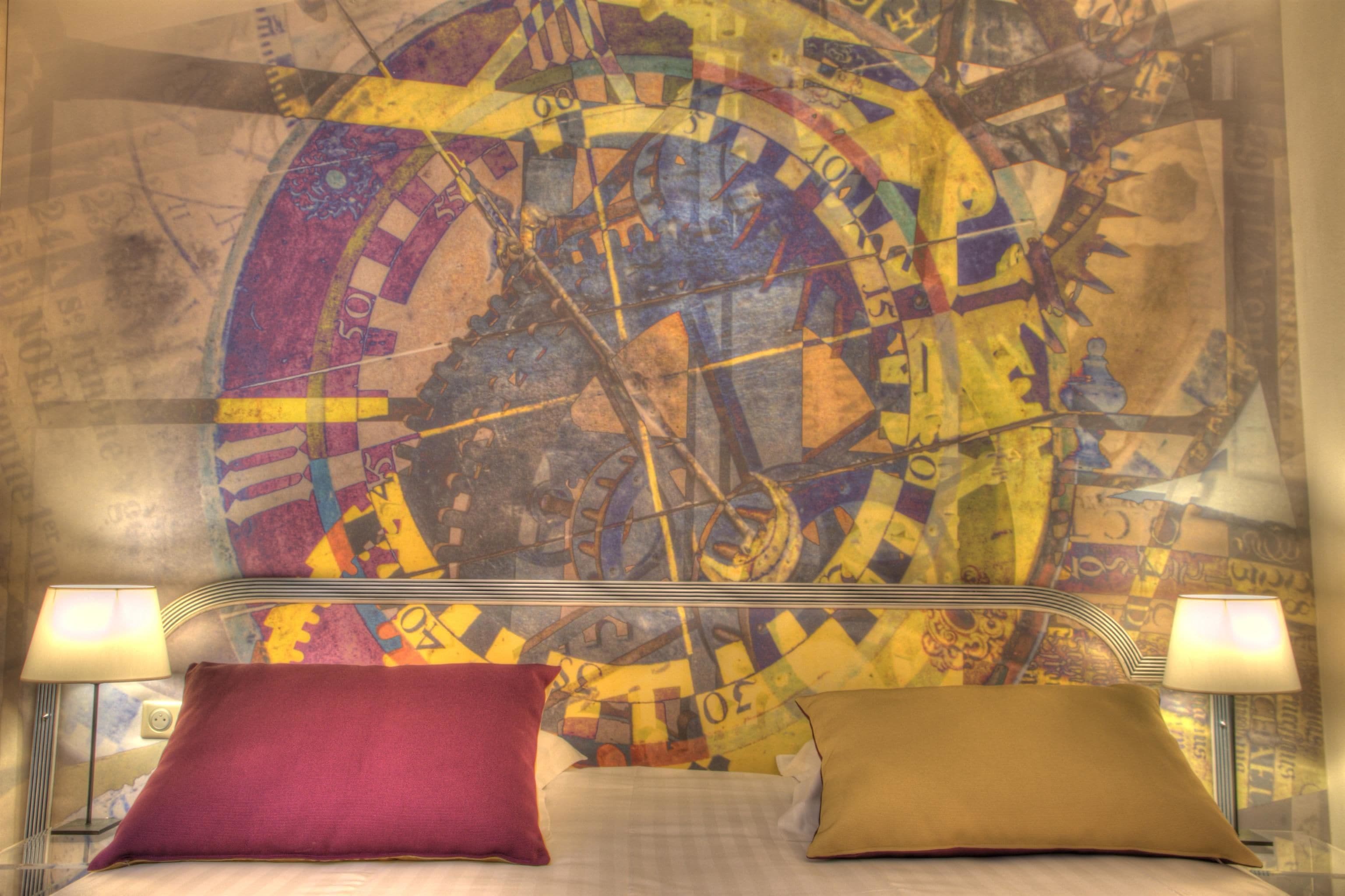 A bed with two pillows, a headboard with a clock, and a wall with a map design.