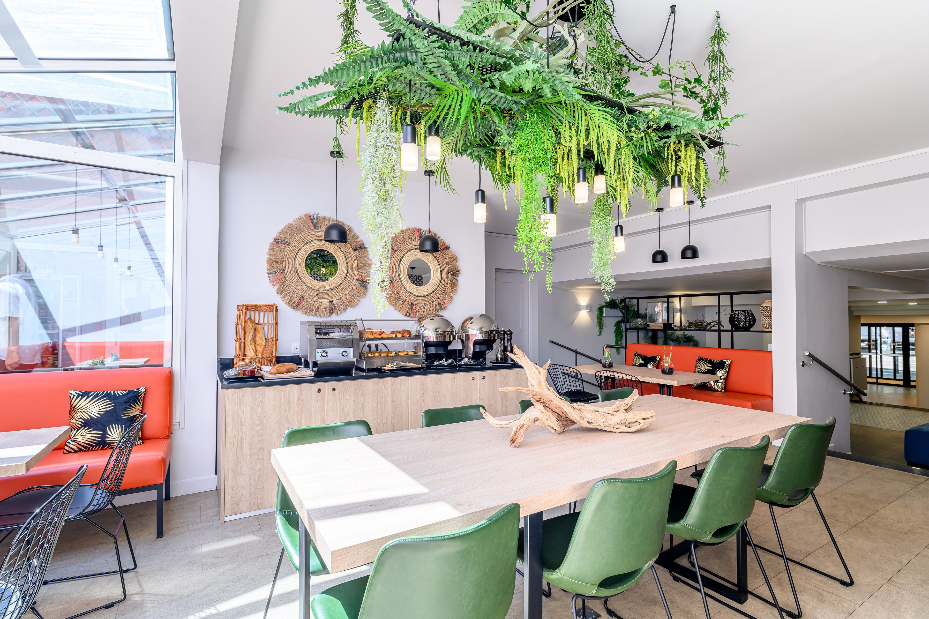 A modern kitchen with a wooden table, green chairs, and hanging plants.