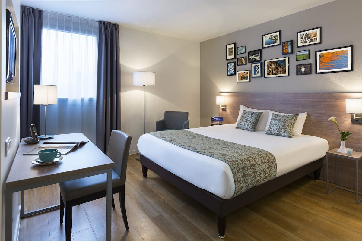 A hotel room with a bed, desk, chair, bedside tables, and a wall with framed pictures.
