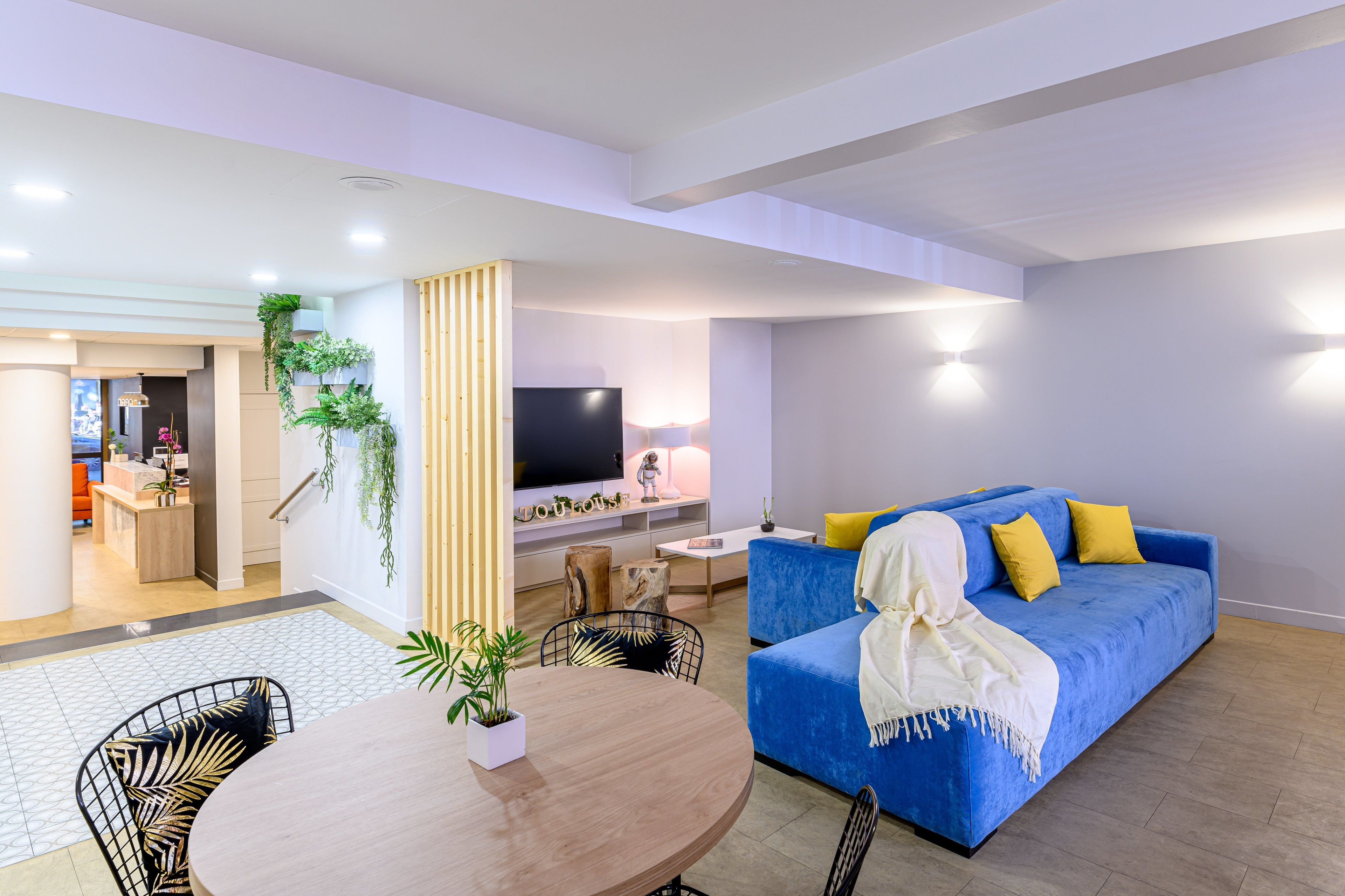 A modern living room with a blue sofa, a wooden dining table, and a TV.