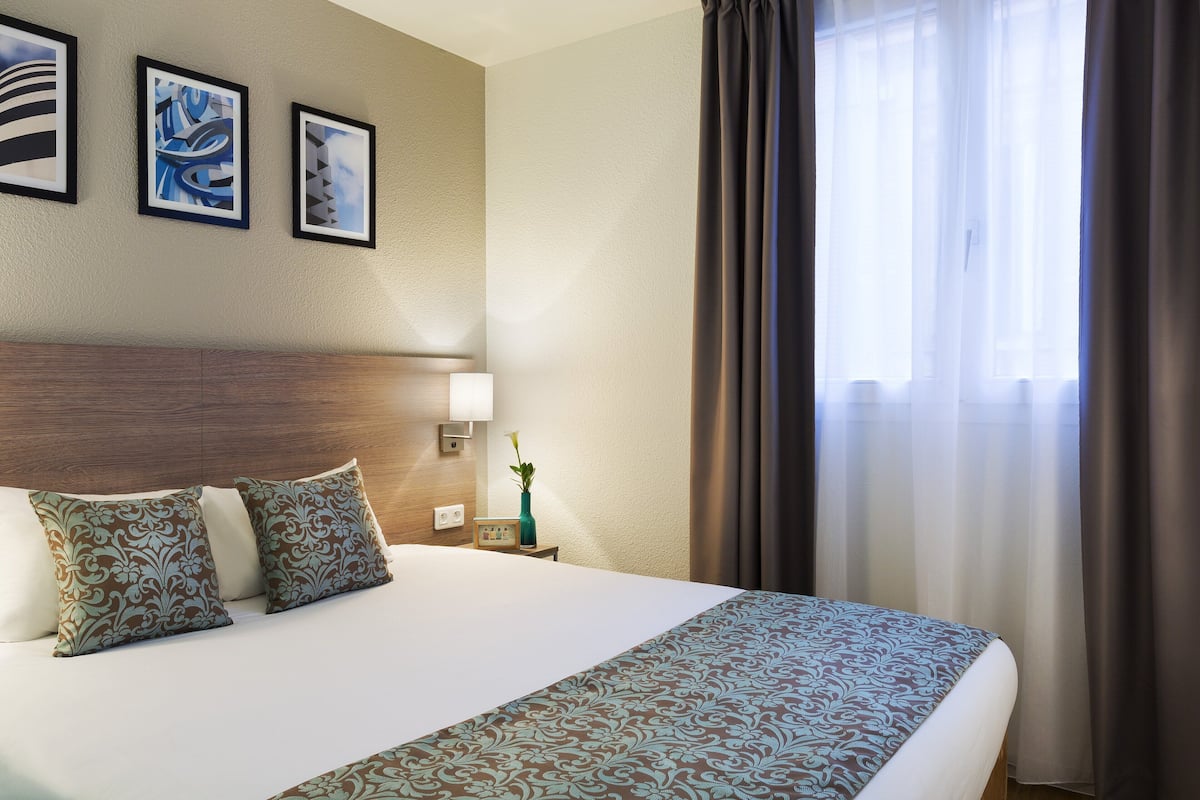 A hotel room with a bed, a nightstand, a lamp, and three framed artworks on the wall.