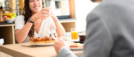 Une personne est assise à une table devant une assiette de nourriture, un verre de jus d’orange et une tasse de café.