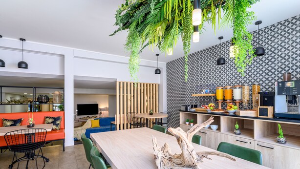 A modern kitchen with a wooden table, green chairs, and hanging plants. - Citadines Wilson Toulouse (Toulouse)