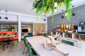 Una cuina moderna amb taula de fusta, cadires verdes i plantes penjants.