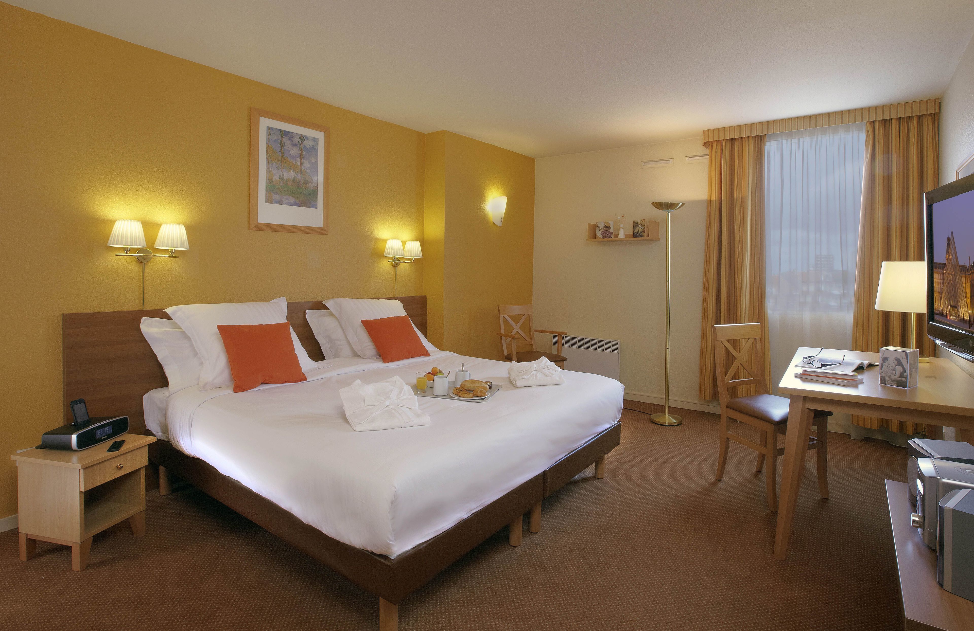 A hotel room with a large bed, bedside lamps, a desk with a chair, and a television.