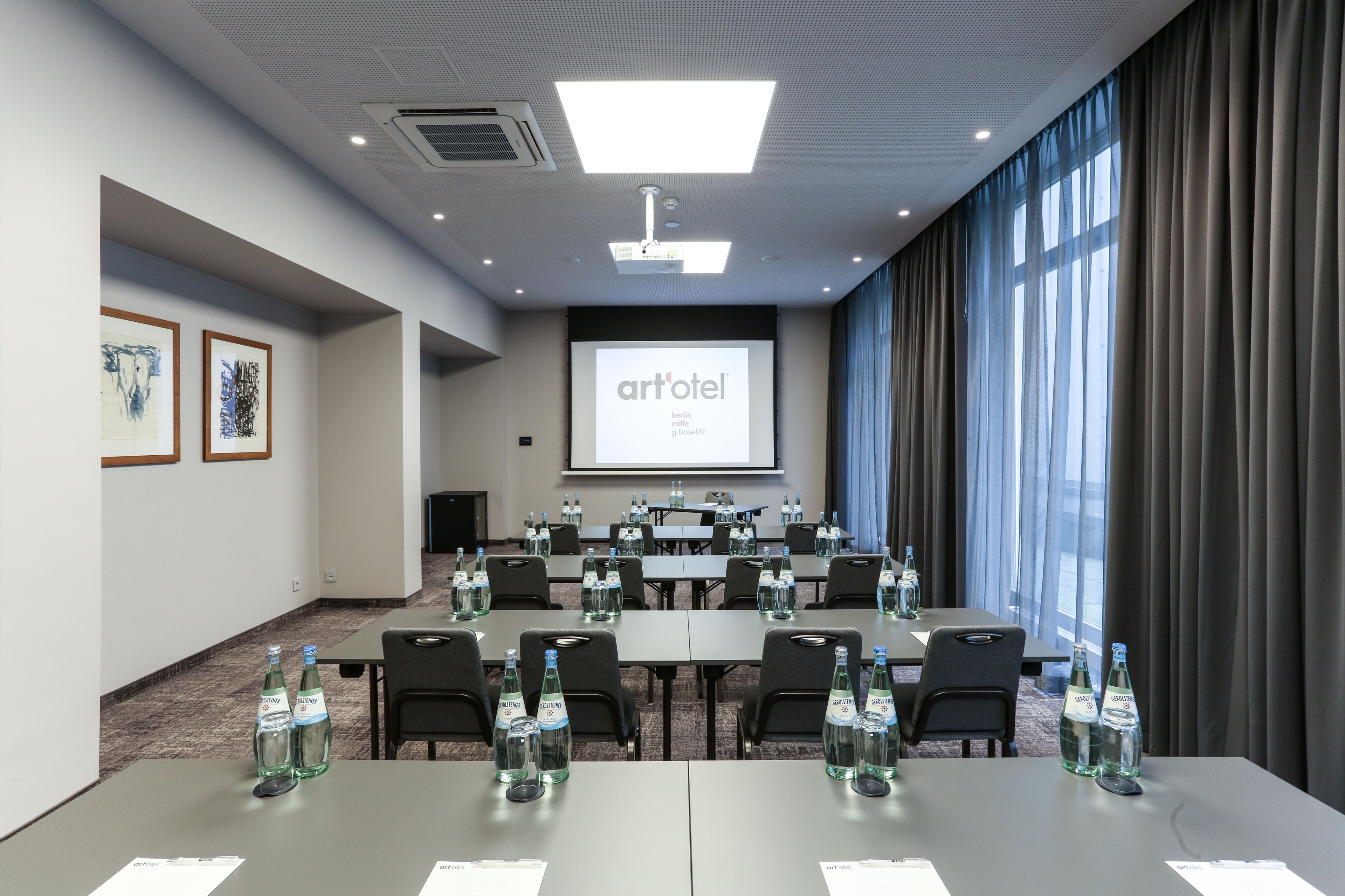 Un salón de conferencias con mesas, sillas y una pantalla proyectora mostrando 'artotel'.