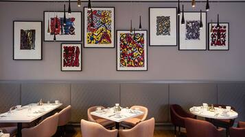 A modern dining area with tables set for service, framed abstract art on the walls, and a clean, contemporary design.