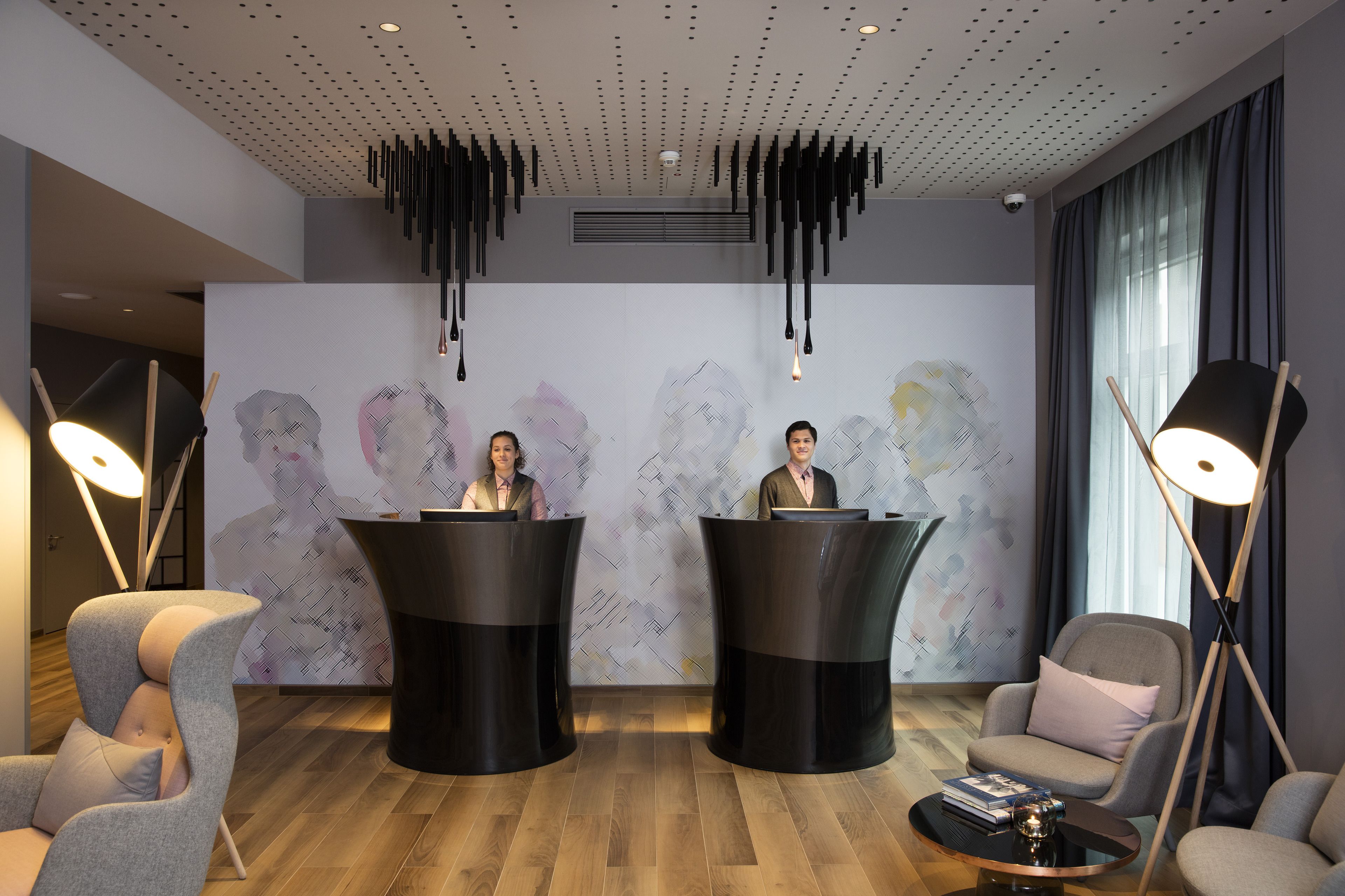 Un vestíbulo moderno con dos mostradores de recepción, un revestimiento mural estampado y mobiliario contemporáneo.