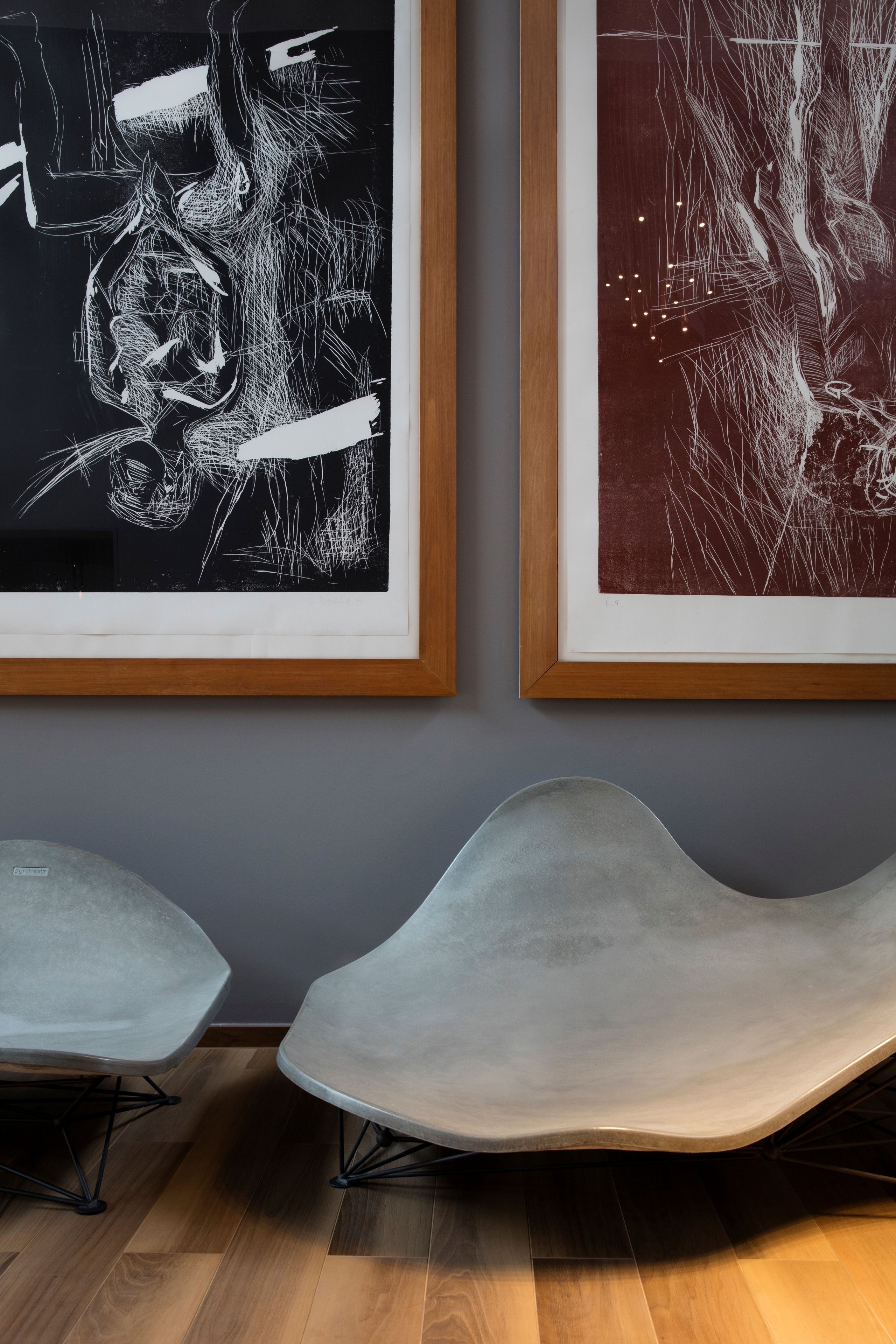 Two framed abstract artworks on a wall, a modern chair in the foreground, and a wooden floor.