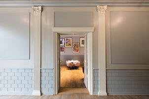A hallway with a dining area, featuring a brick wall, white columns, and a wooden floor.
