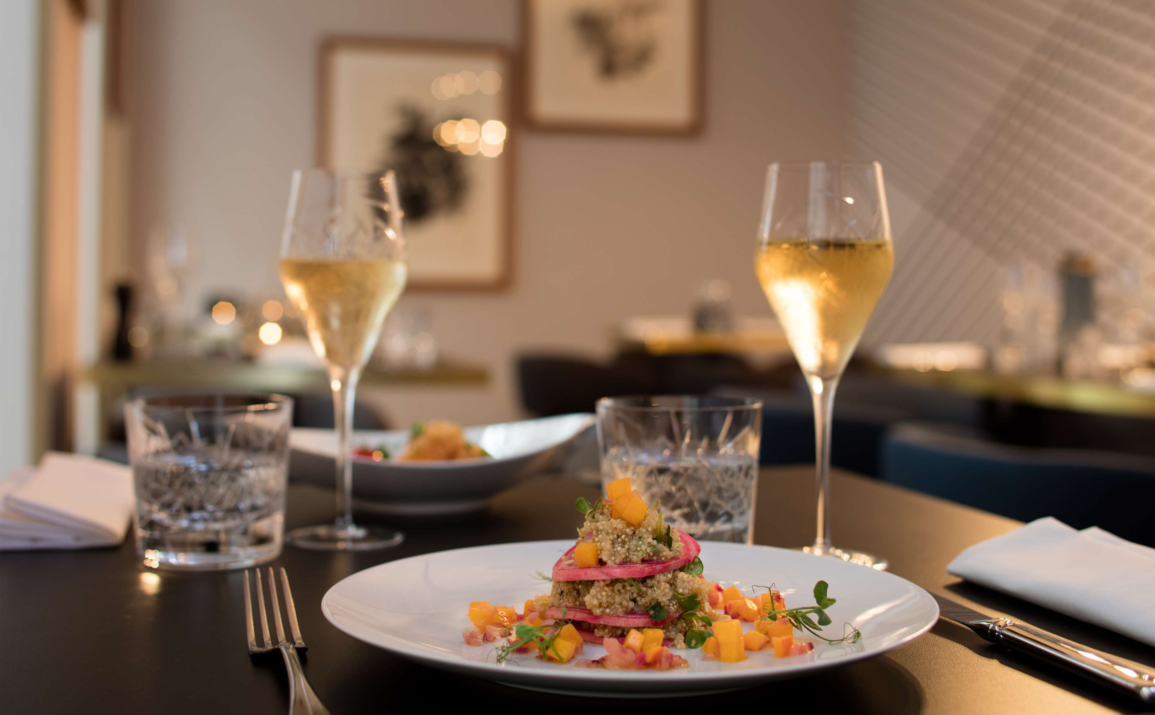 Une table à manger avec une assiette de nourriture, deux verres de vin blanc et une fourchette.