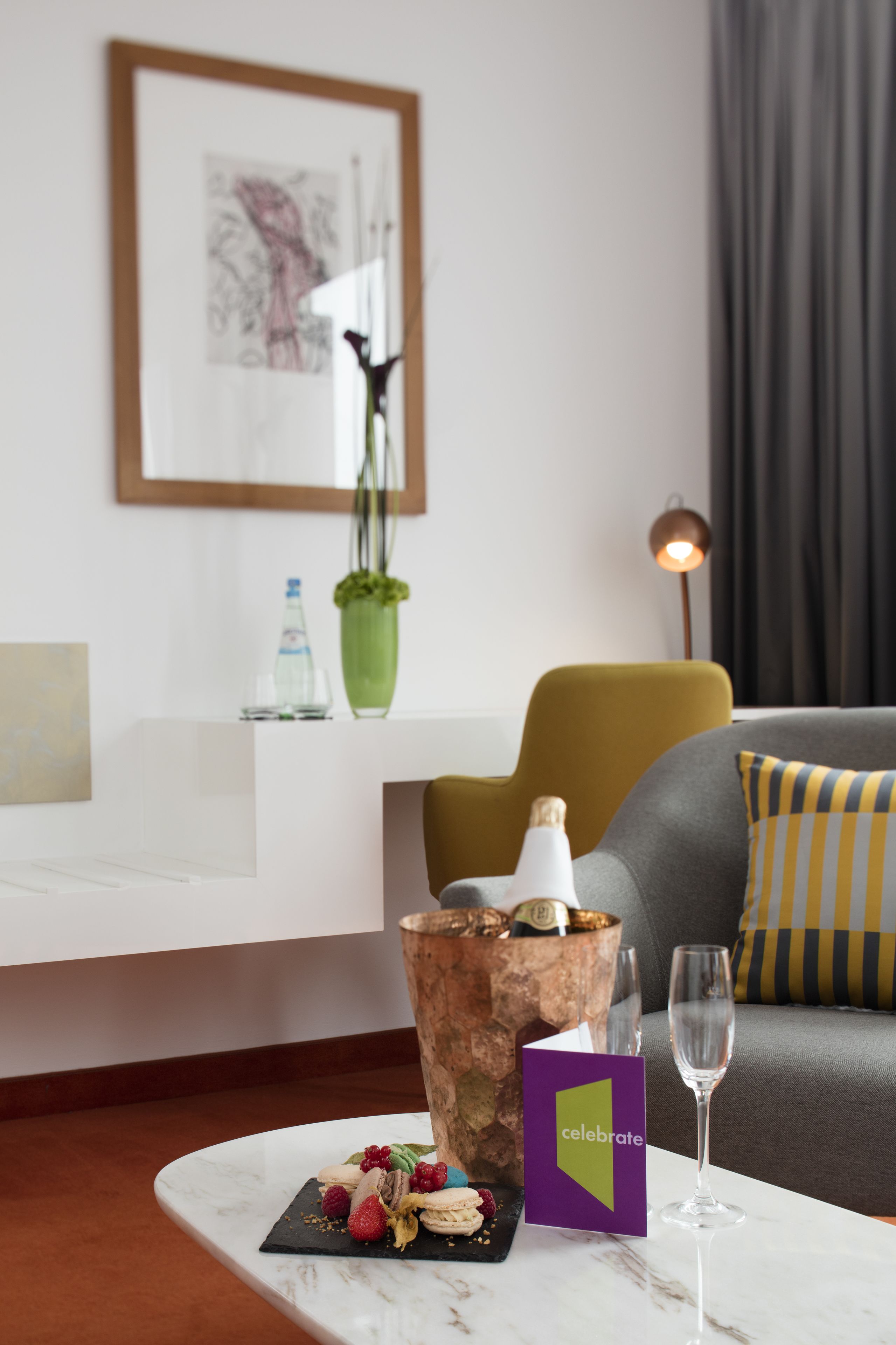A modern living room with a marble coffee table, a framed artwork on the wall, a green vase, and a sofa with striped cushions.