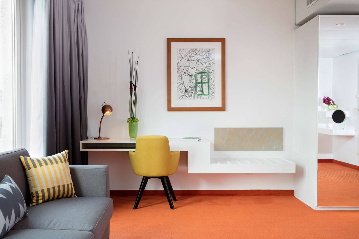 A modern room with a grey sofa, a yellow chair, a desk, and a framed artwork on the wall.