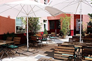 An outdoor cafe with wooden tables and chairs, white umbrellas, and potted plants.