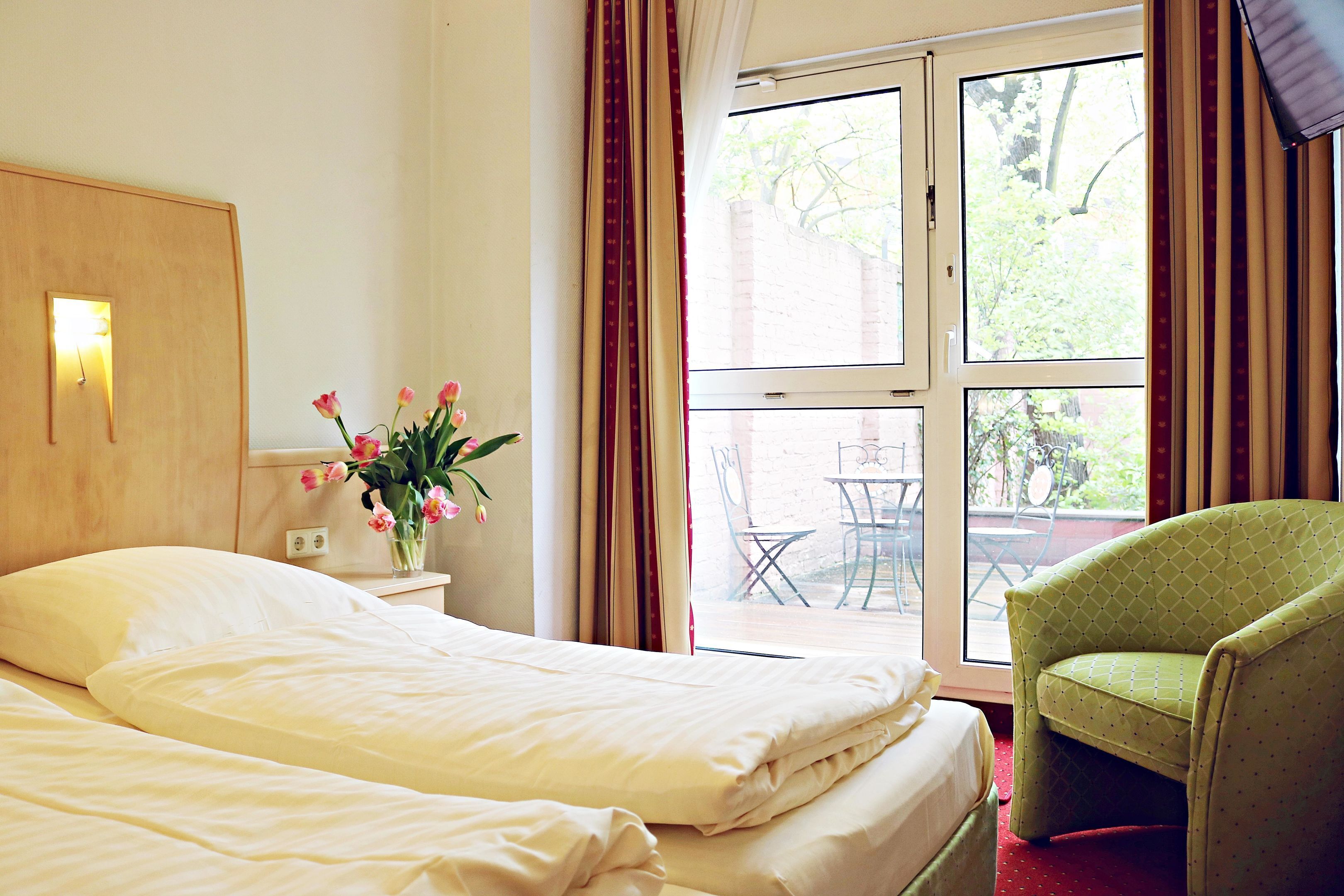 A hotel room with a bed, a chair, a table, and a window with curtains.