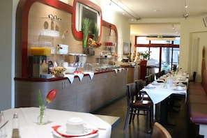 Un ristorante con un lungo bancone, diversi tavoli e un'ampia scelta di pietanze esposte.
