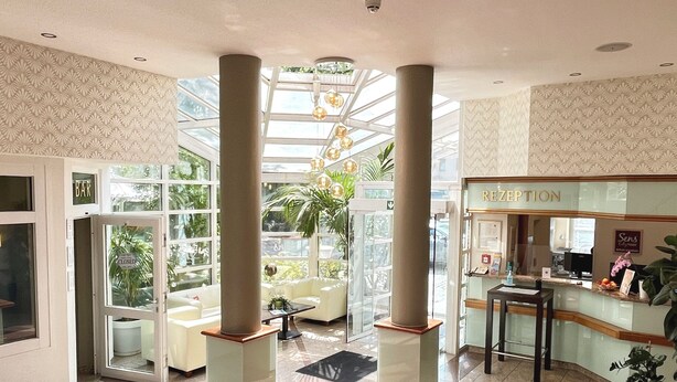 Um saguão de hotel com balcão de recepção, área de estar e entrada por porta de vidro.
