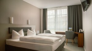 Quarto de hotel com uma cama grande, uma escrivaninha, uma cadeira e televisão na parede.
