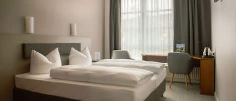 A hotel room with a large bed, a desk, a chair, and a TV mounted on the wall.