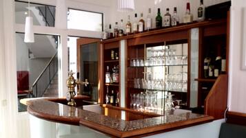 Un coin bar doté d’un comptoir en granit, d’étagères remplies de bouteilles et de verres, et d’un escalier en arrière-plan.