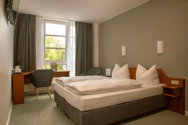 A hotel room with a large bed, a desk, a chair, and a window with curtains. - SensCity Hotel Berlin Spandau (Berlin)