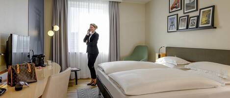Habitación de hotel con una cama, un escritorio con computadora, una silla, cafetera y ventana con cortinas.
