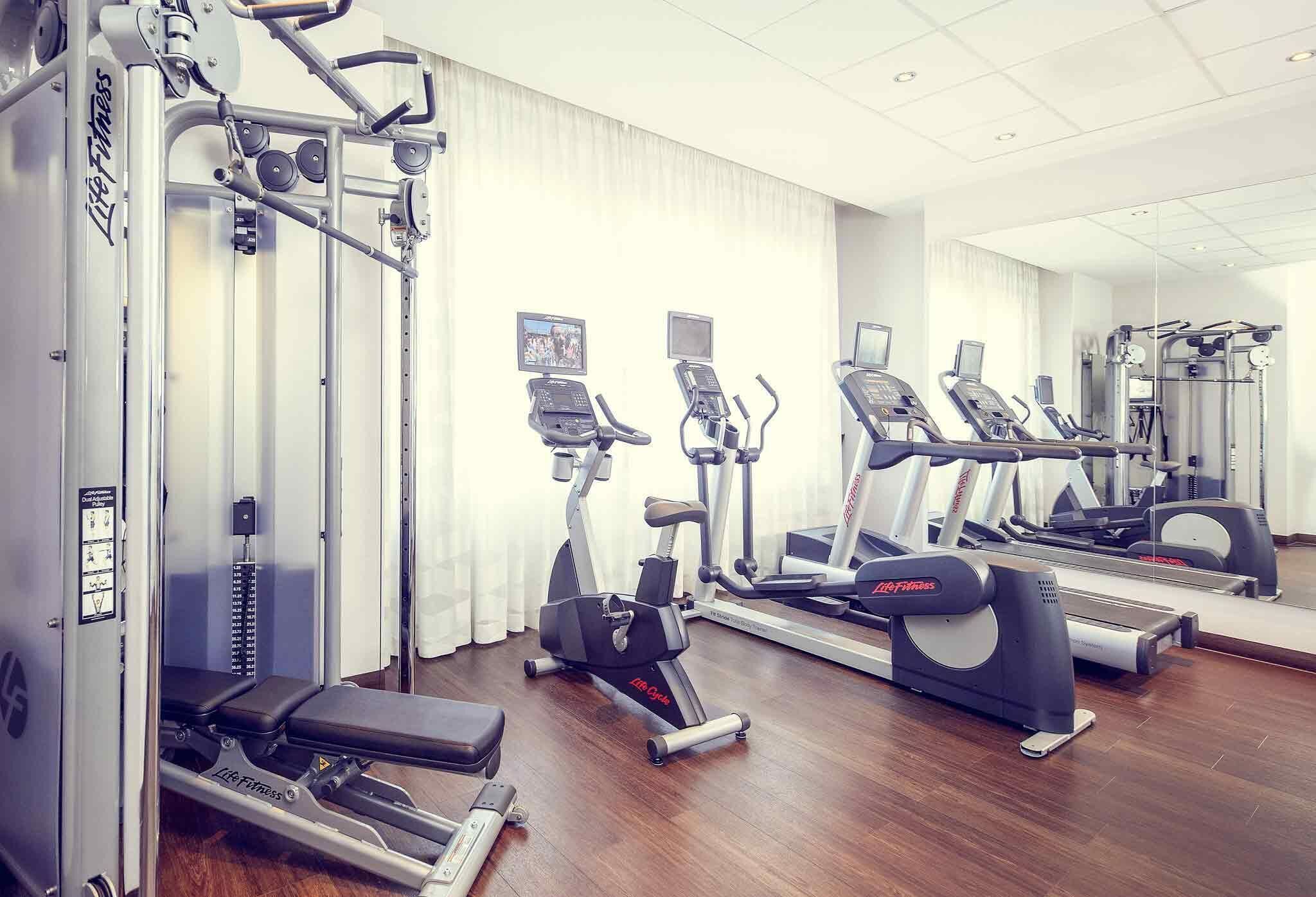 Ein Fitnessraum mit Cardiogeräten, Krafttrainingsgeräten und einer Spiegelwand.