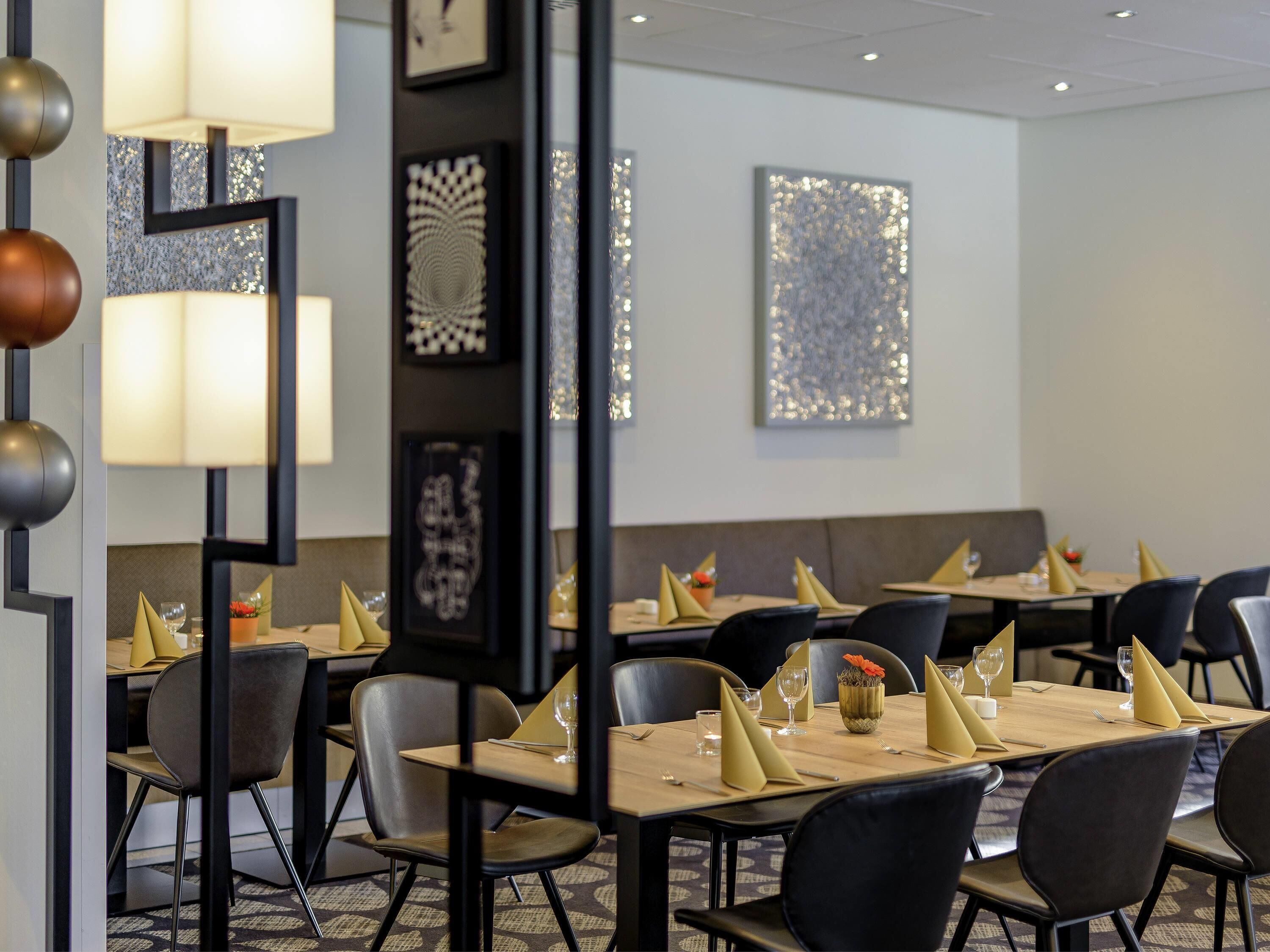 A dining area with tables set for service, framed artwork on the walls, and modern lighting fixtures.