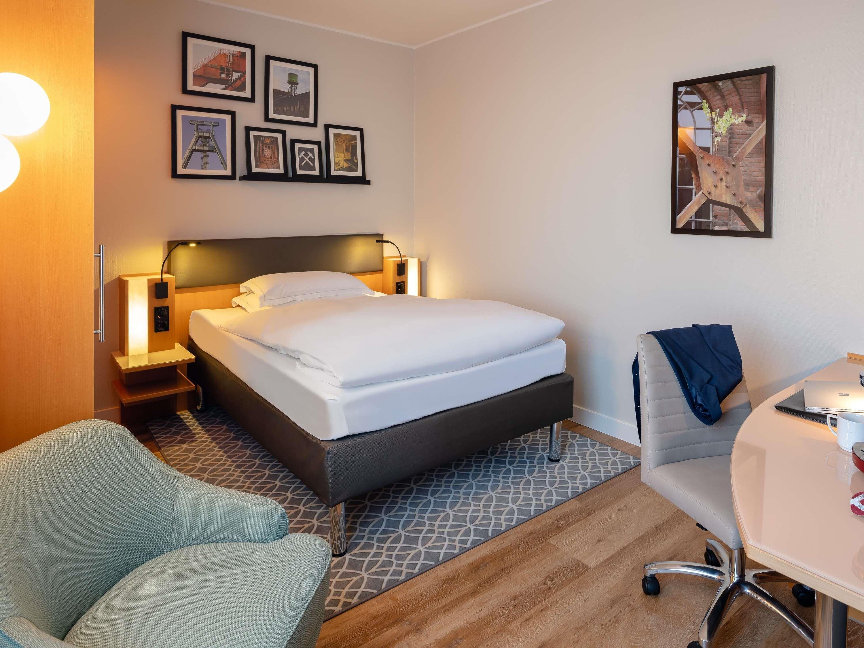 Une chambre d’hôtel comprenant un lit, des tables de chevet, un bureau, une chaise et un mur décoré de tableaux encadrés.