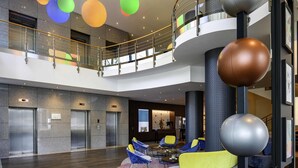 A modern lobby with a central seating area, elevators, and a mezzanine level with a balcony.