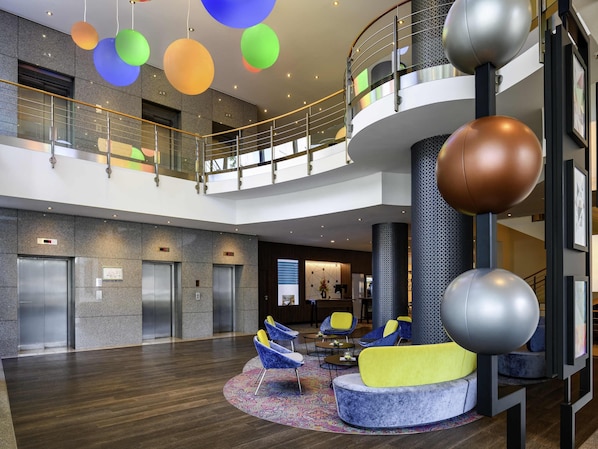 Eine moderne Lobby mit einer zentralen Sitzecke, Aufzügen und einer Empore mit einem Balkon.