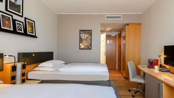 Ett hotellrum med två sängar, ett skrivbord med en dator, en tv och inramade tavlor på väggen.