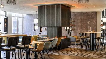 A modern restaurant with high ceilings, pendant lighting, and a central fire feature.