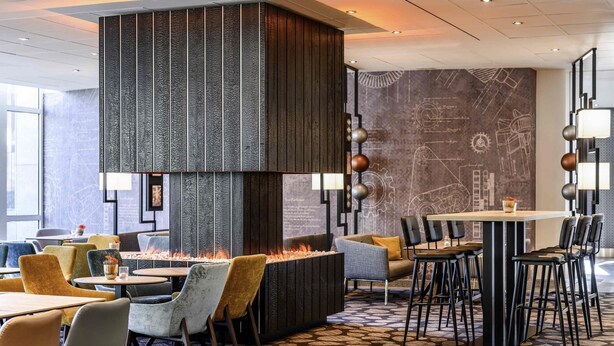 A modern dining area with a central fire feature, multiple seating options, and a patterned floor.