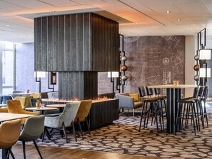 A modern dining area with a central fire feature, multiple seating options, and a patterned floor.