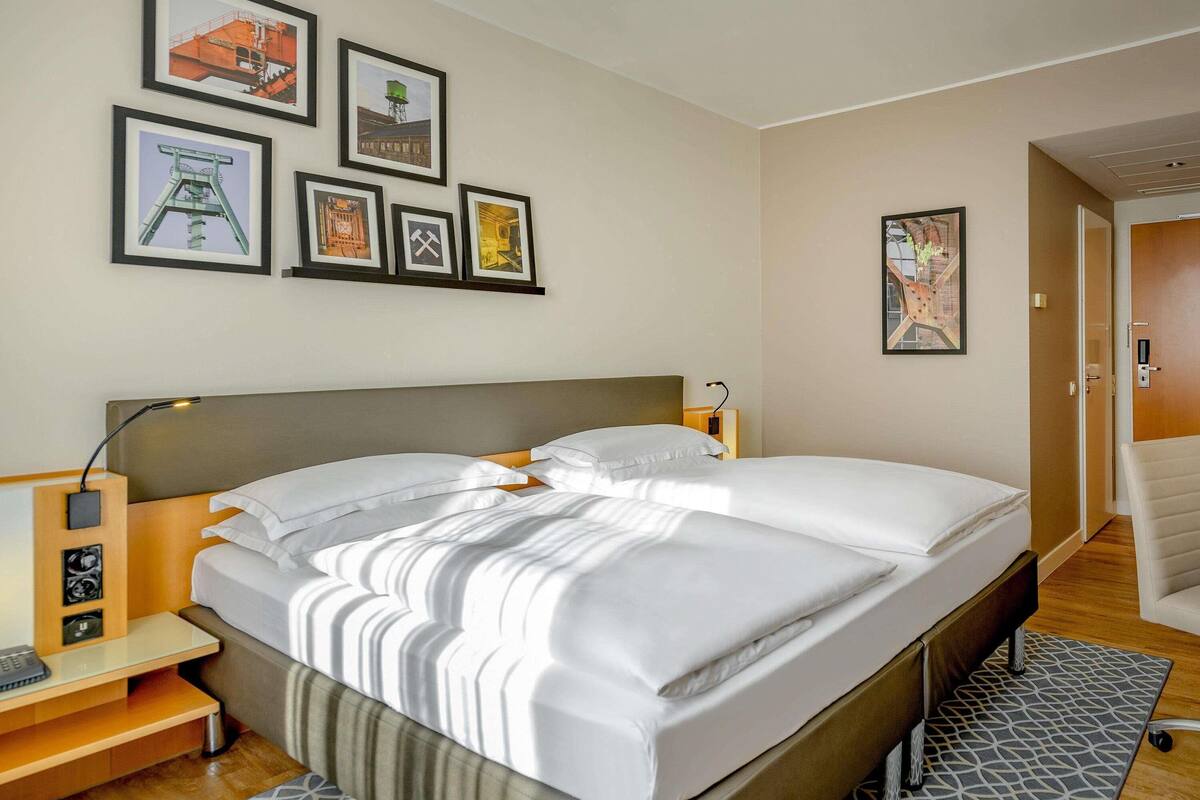 Une chambre d’hôtel avec un lit, des tables de chevet, un bureau, une chaise et des tableaux encadrés au mur.
