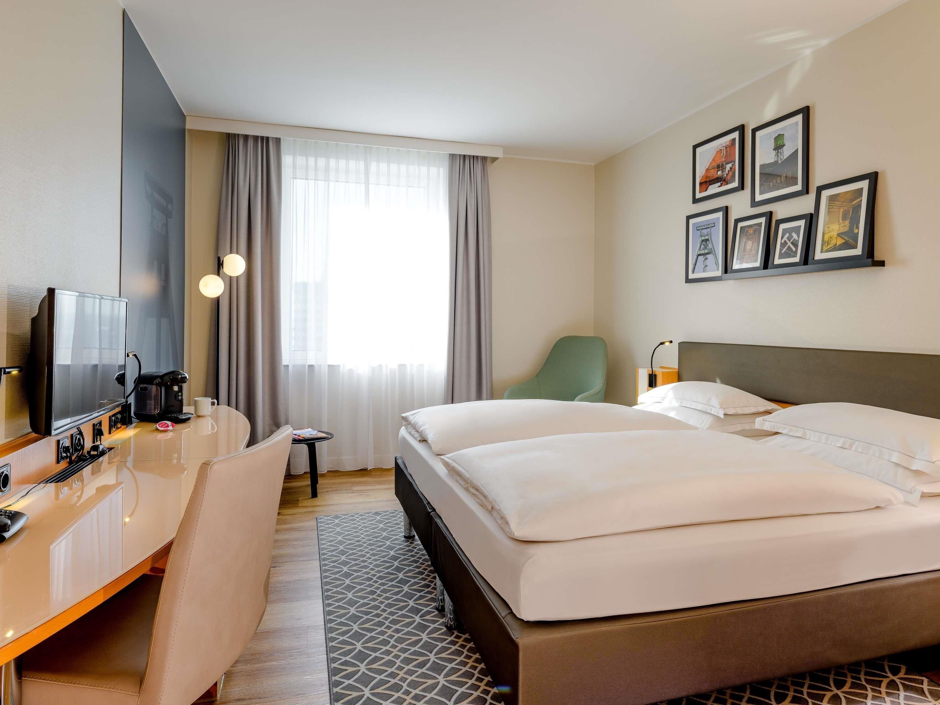 Une chambre d’hôtel avec un lit, un bureau doté d’une machine à café, une chaise, un téléviseur et des tableaux encadrés au mur.