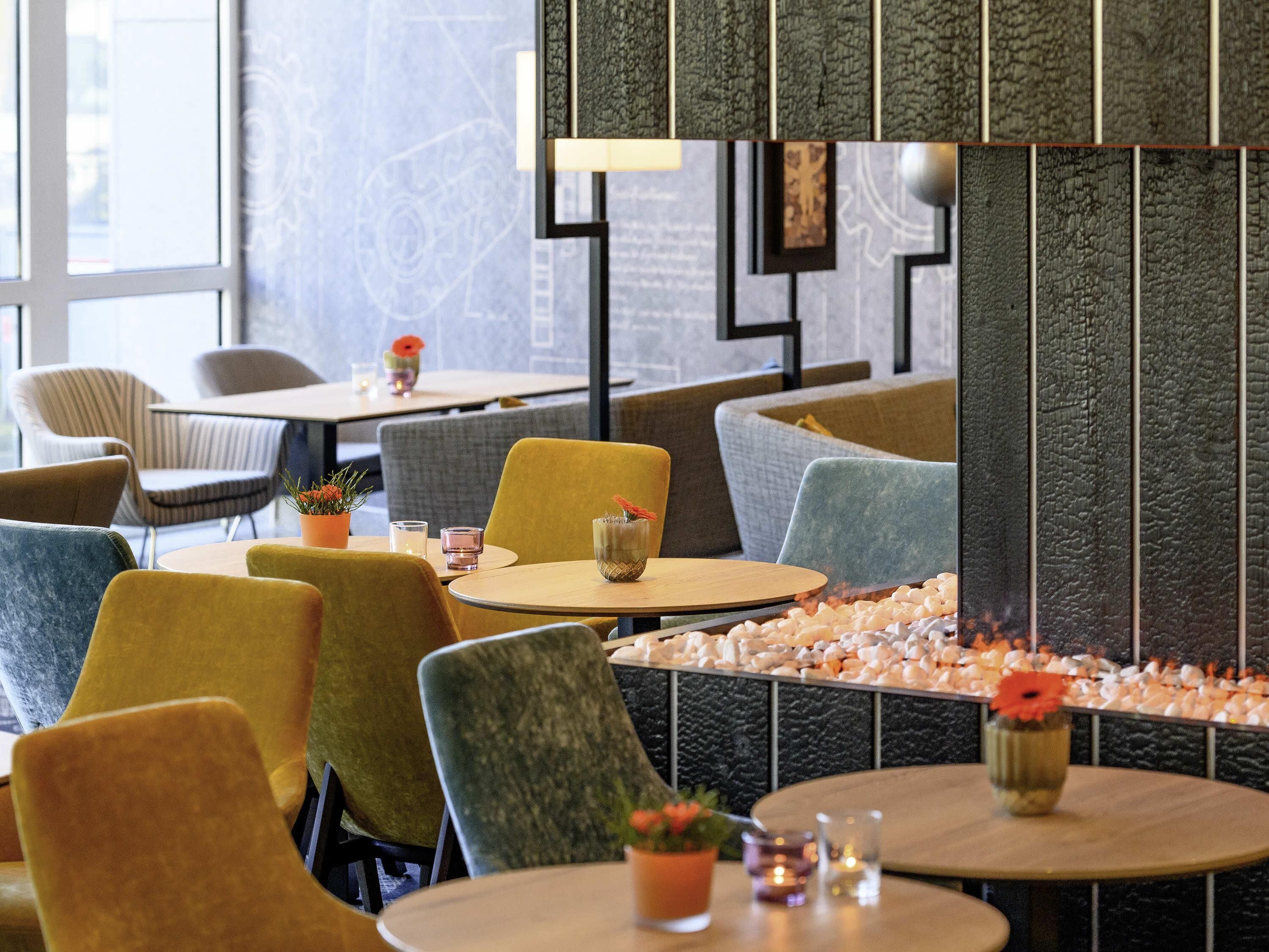 A modern restaurant interior with round tables, cushioned chairs, and a decorative wall.