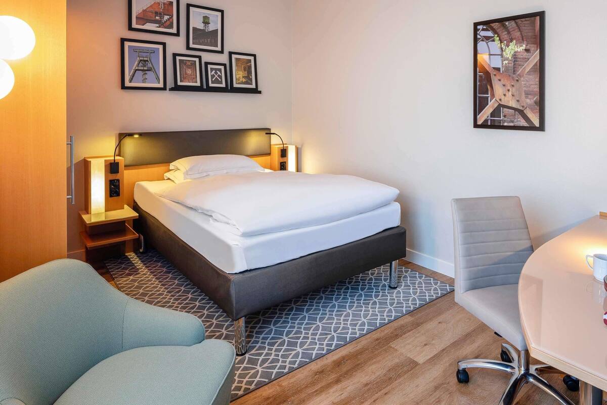 Une chambre d’hôtel avec un lit, un bureau, une chaise et un mur orné de tableaux.
