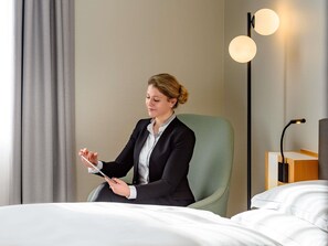 Una persona sentada en una habitación con una cama, una lámpara y un aplique de pared.